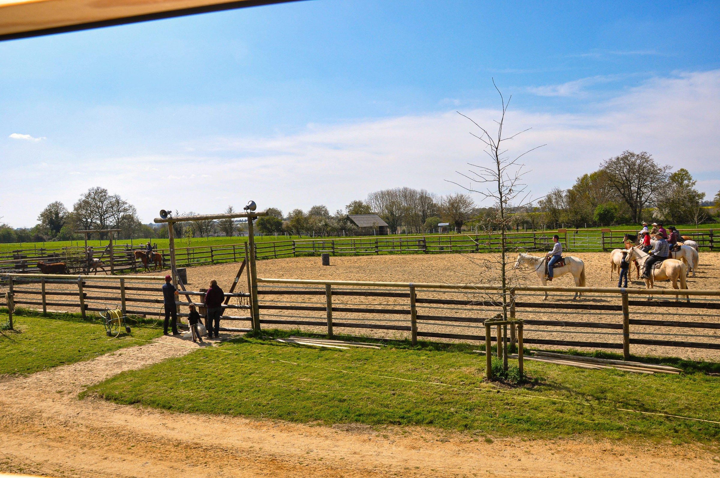 The ranch’s outdoor arena, with wooden fencing and riders in the distance