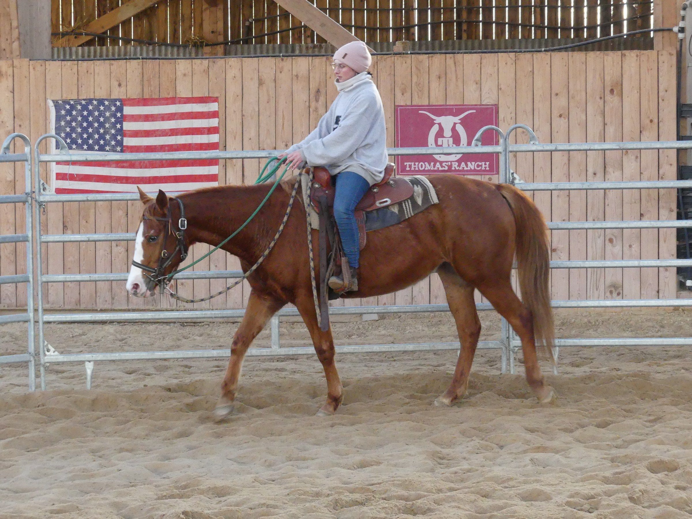 Rider in a western saddle walking on a sorrel horse, in front of the American flag and the ranch sign