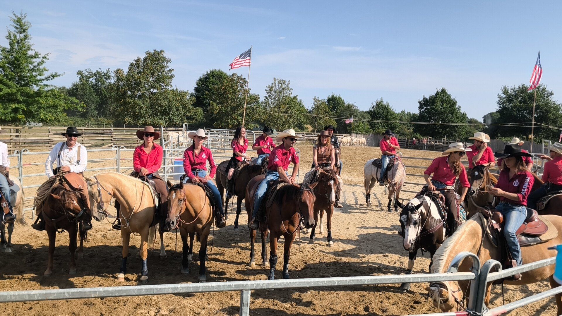 Cavalières et cavaliers du ranch en chemise rouge, alignés à cheval dans le rond, drapeaux américains au-dessus de la carrière
