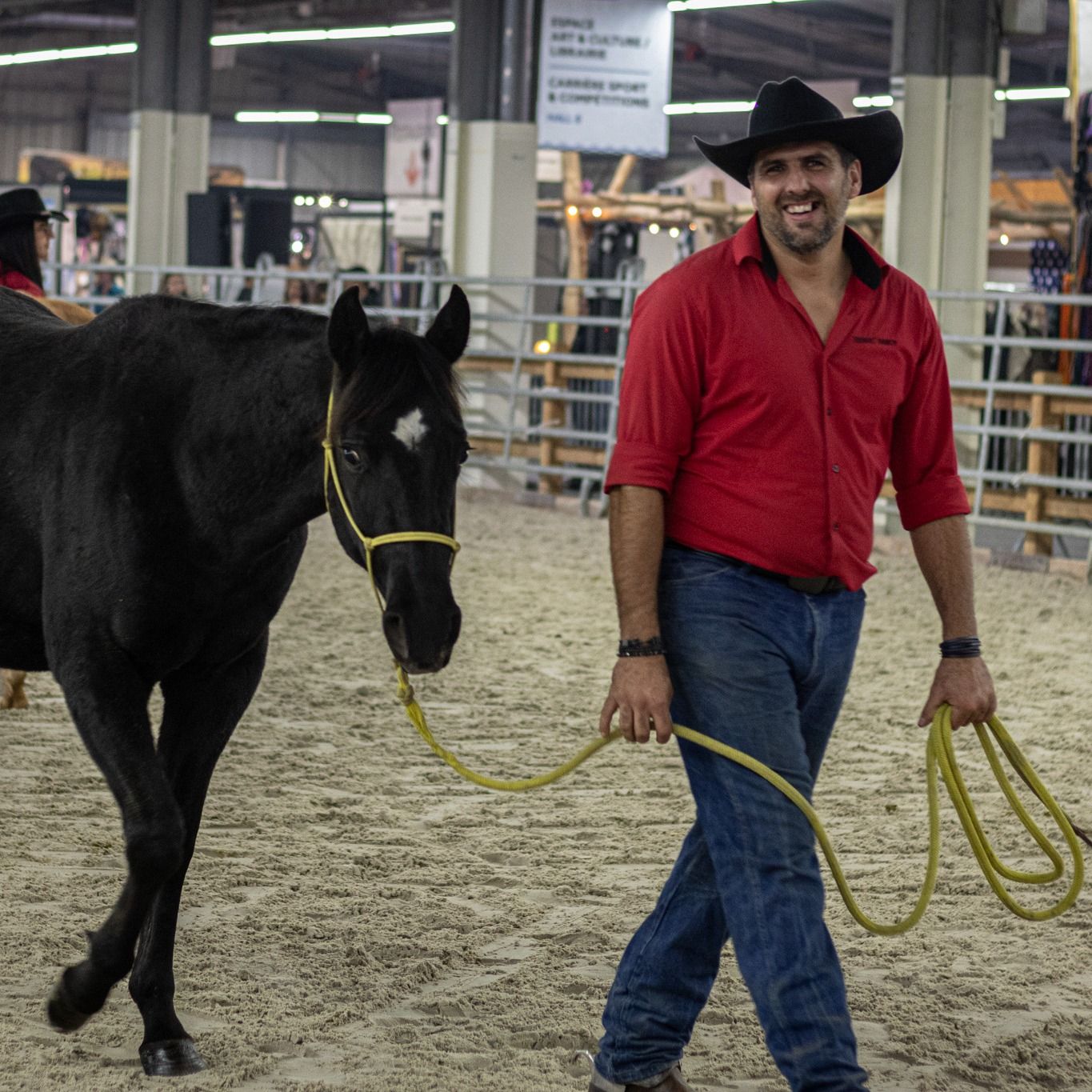 Cavalier en chemise rouge brodée du ranch menant un cheval noir en main, au salon