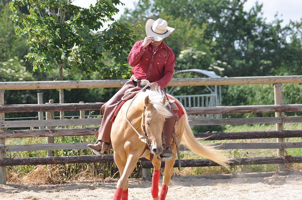 Cavalier western en chemise rouge sur un cheval palomino, dans la carrière du ranch