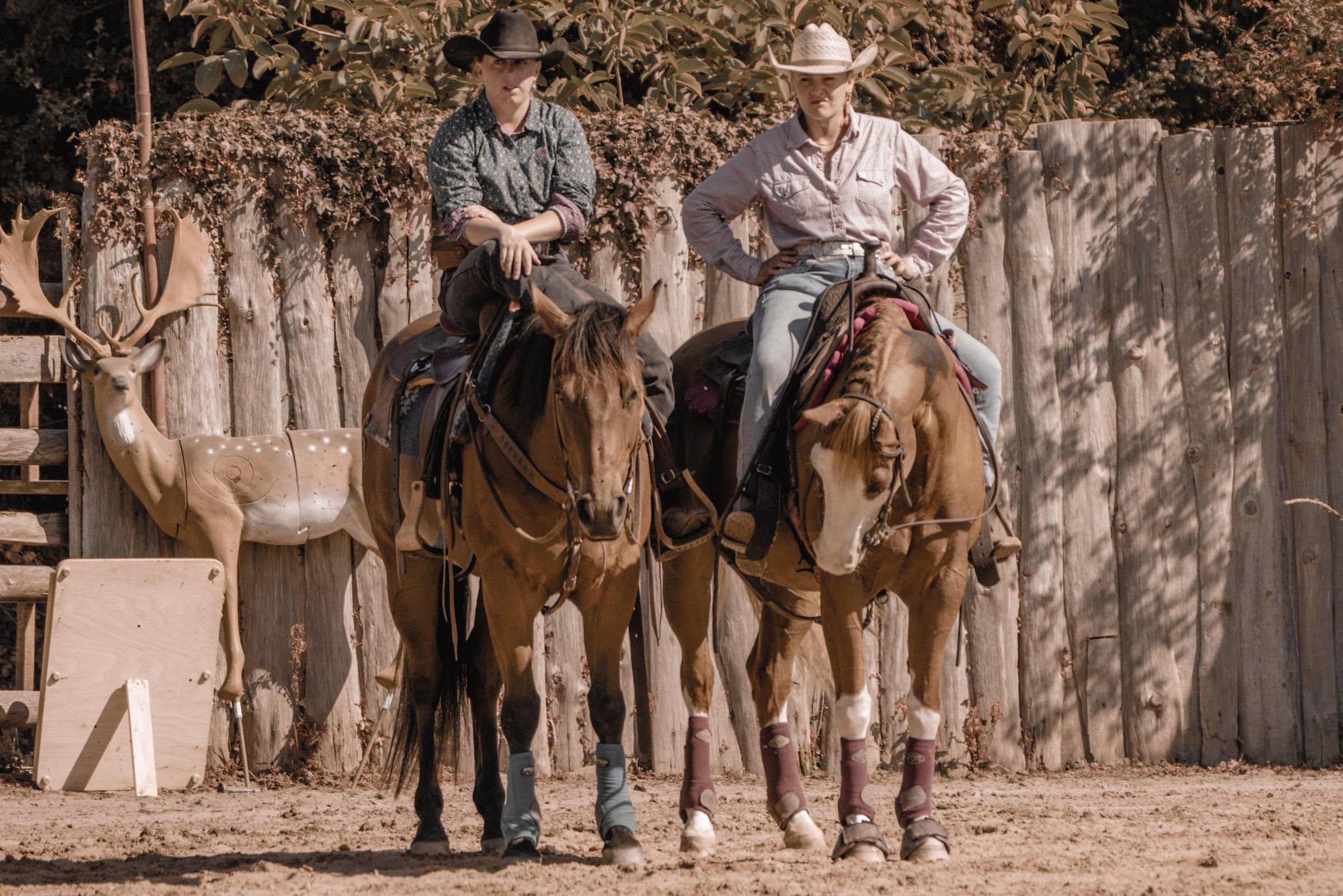 Deux cavaliers western en chapeau, à cheval devant une palissade du ranch