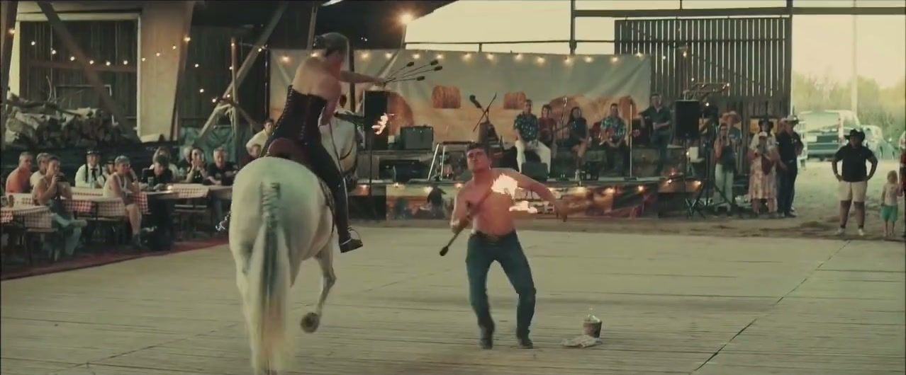 Cavalière sur un cheval blanc et artiste de feu en spectacle sur le parquet du manège, devant les tablées