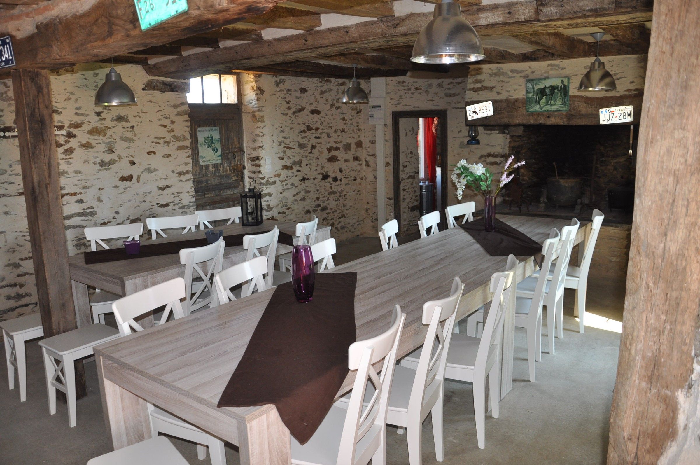 Pièce de vie aux murs en pierre d’un gîte du ranch, longues tables et chaises blanches