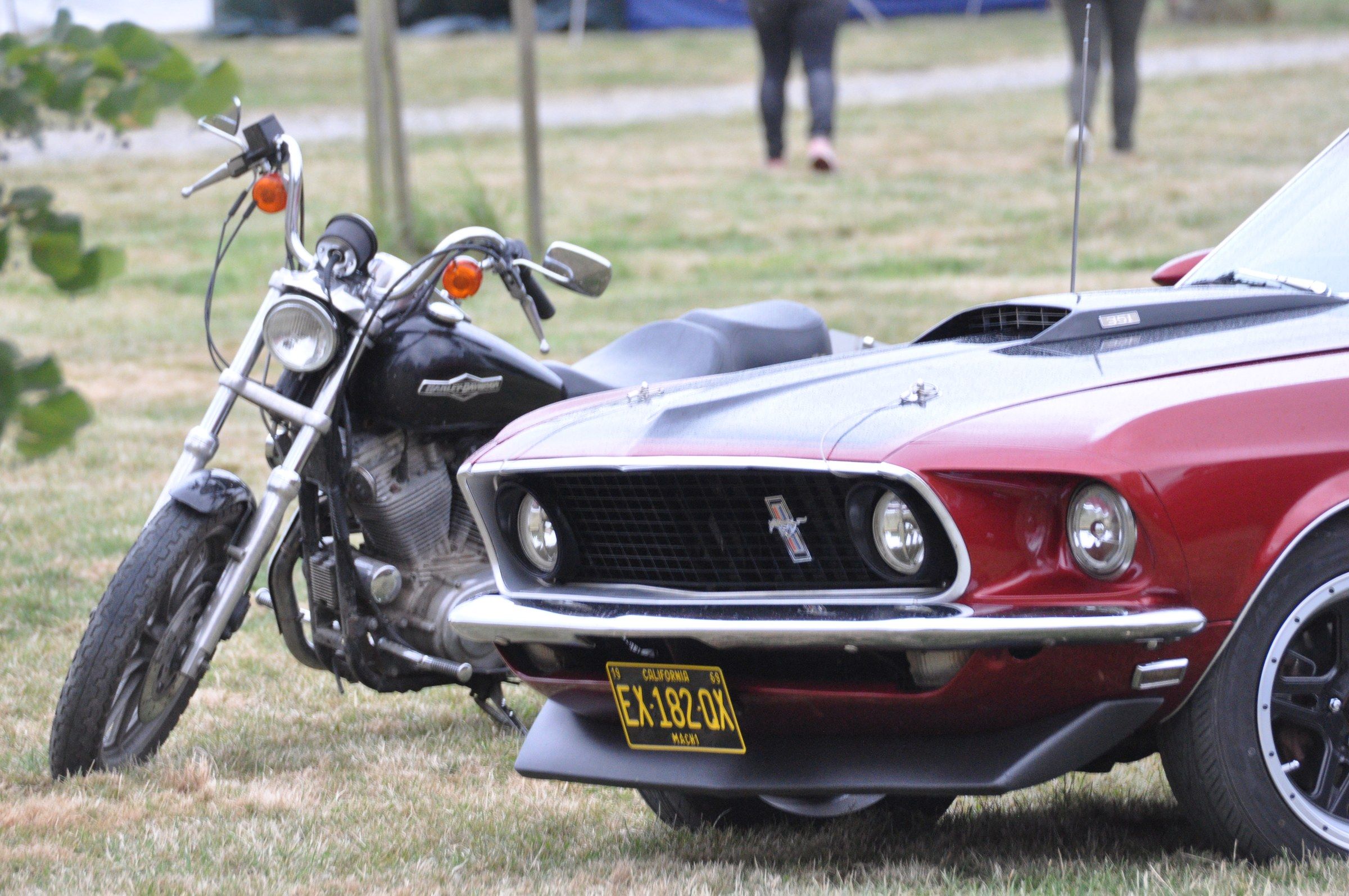 Moto Harley-Davidson et Ford Mustang rouge exposées sur la pelouse du ranch