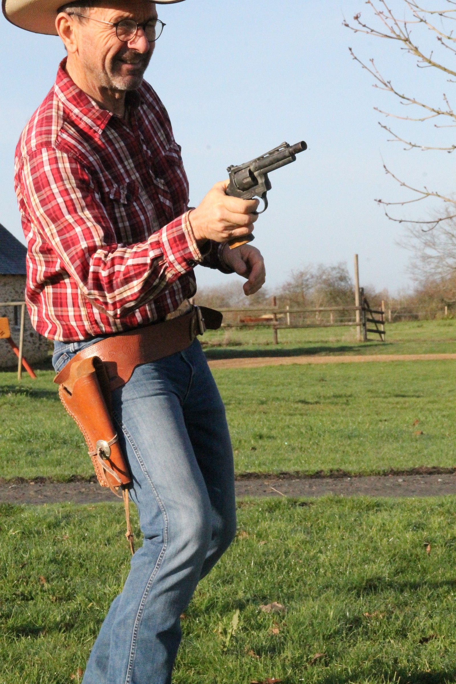 Jacky Thomas dégaine un pistolet de son holster dans un pré du ranch, en riant