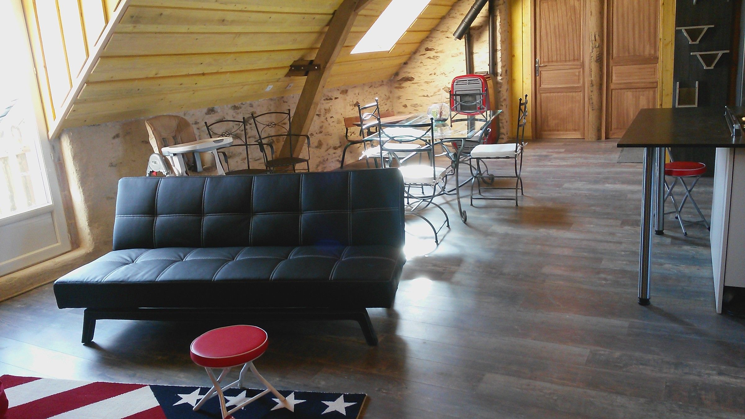 Le salon du Loft sous les combles, canapé noir et tapis au drapeau américain
