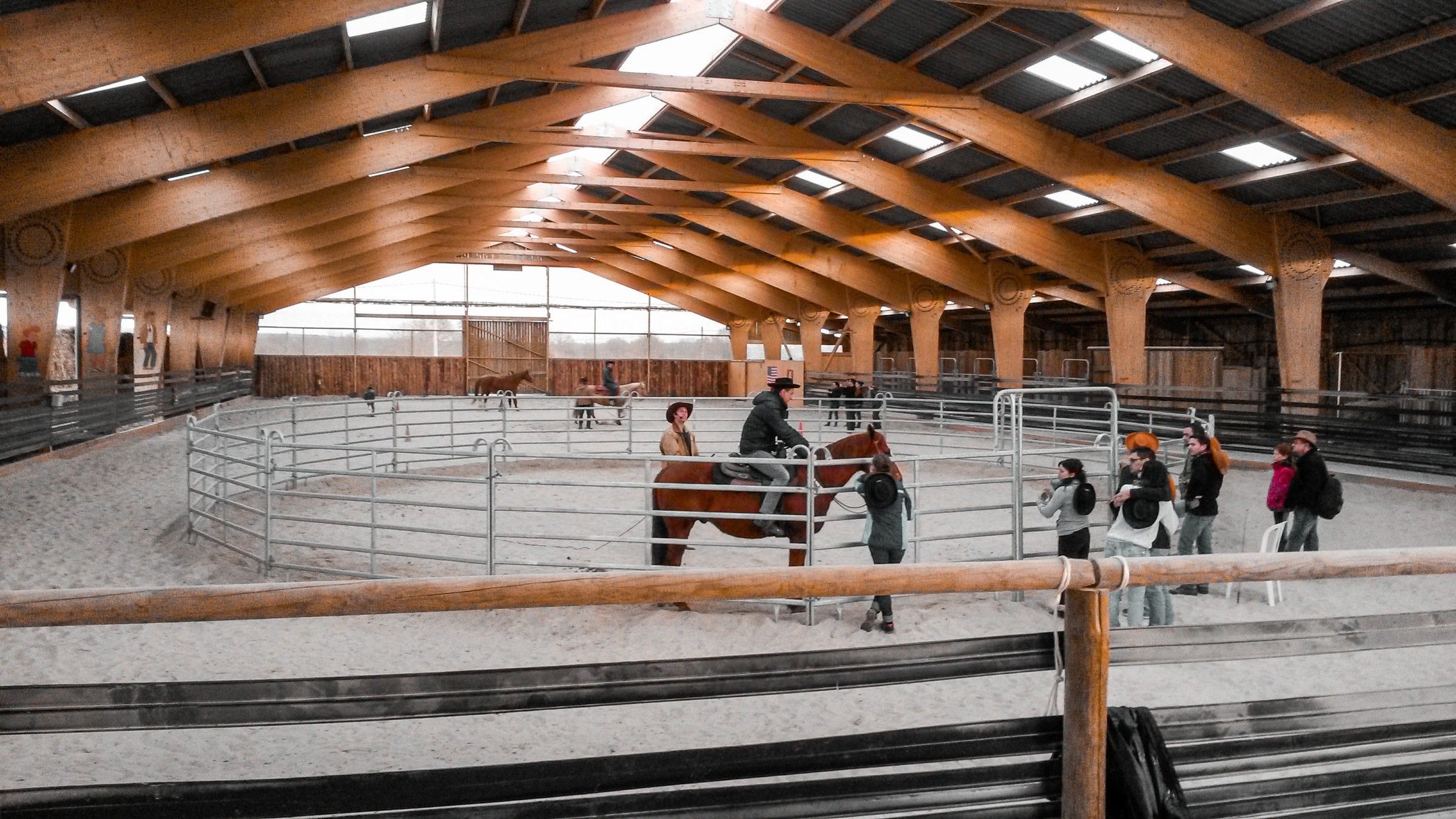 Le manège couvert du ranch, un rond de travail en barrières, un cavalier et des visiteurs à pied
