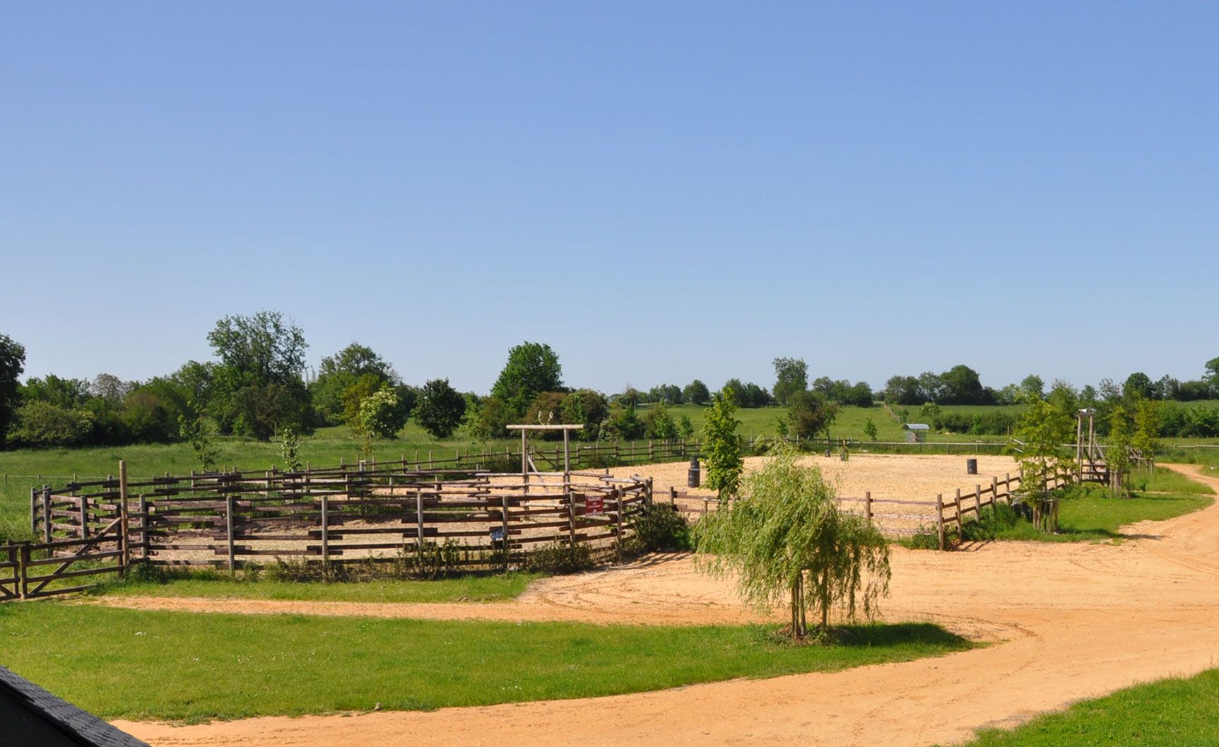 Le rond de longe en bois du ranch, un saule et les prés sous un ciel bleu