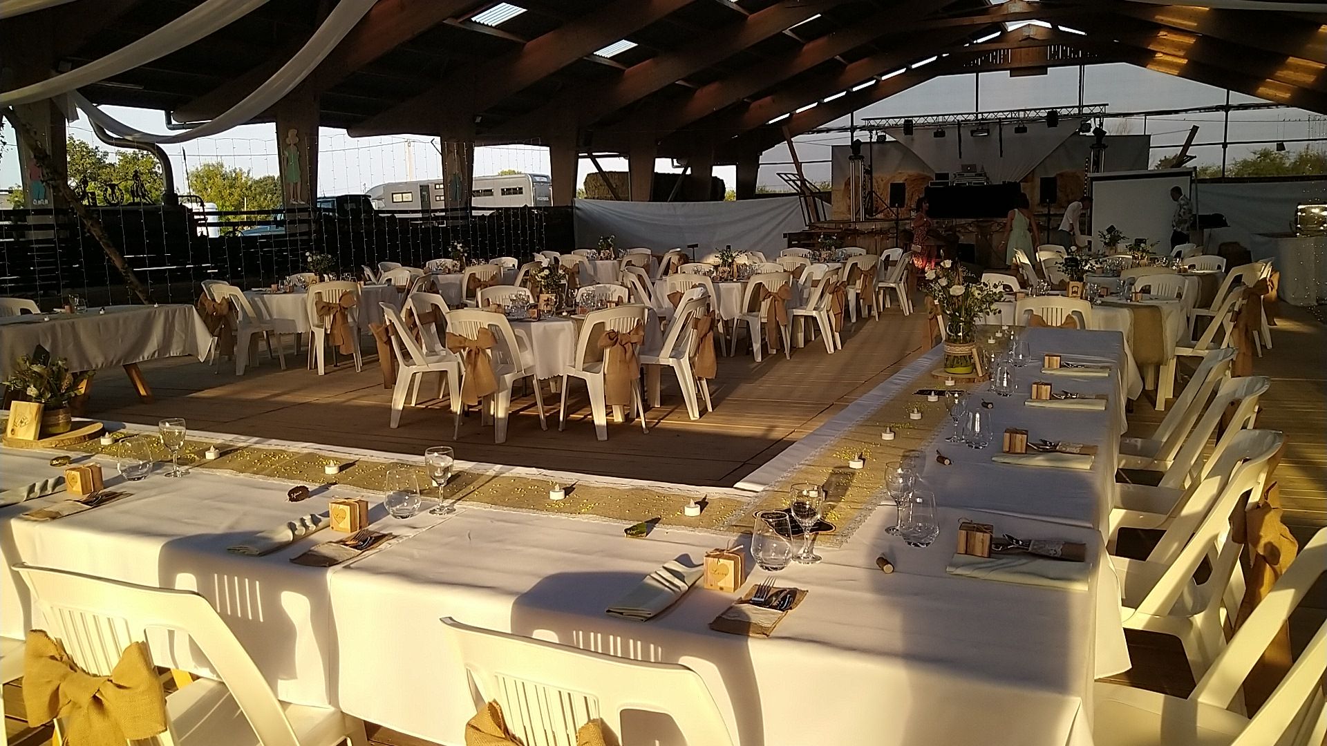 Grande salle dressée pour un mariage, tables nappées et chaises blanches sous la charpente