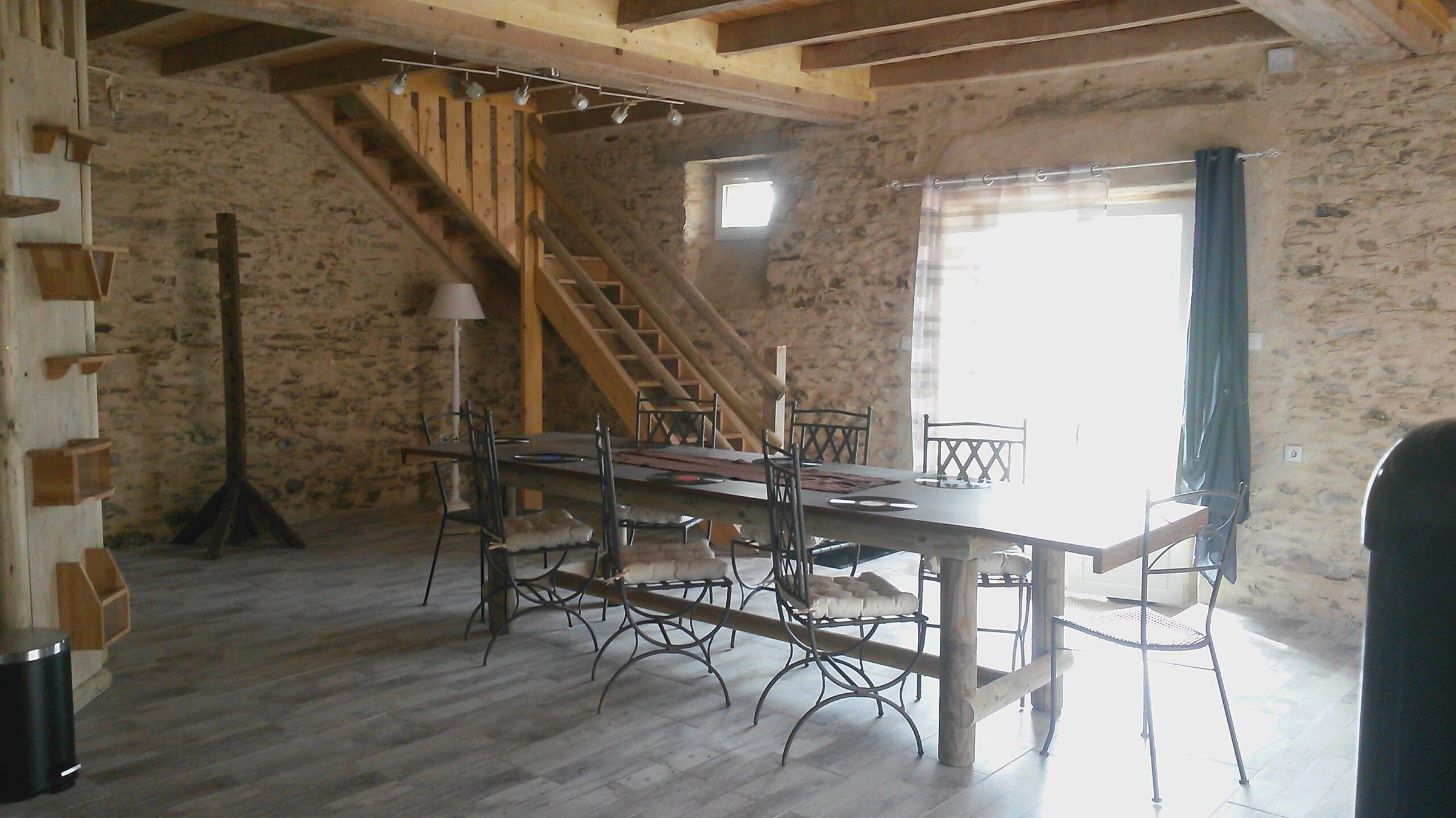 La pièce de vie de la Sellerie : murs en pierre, grande table et escalier en bois