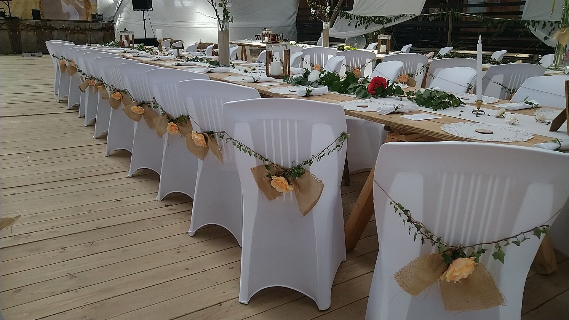 Longue tablée de mariage, chaises blanches nouées de jute et de verdure