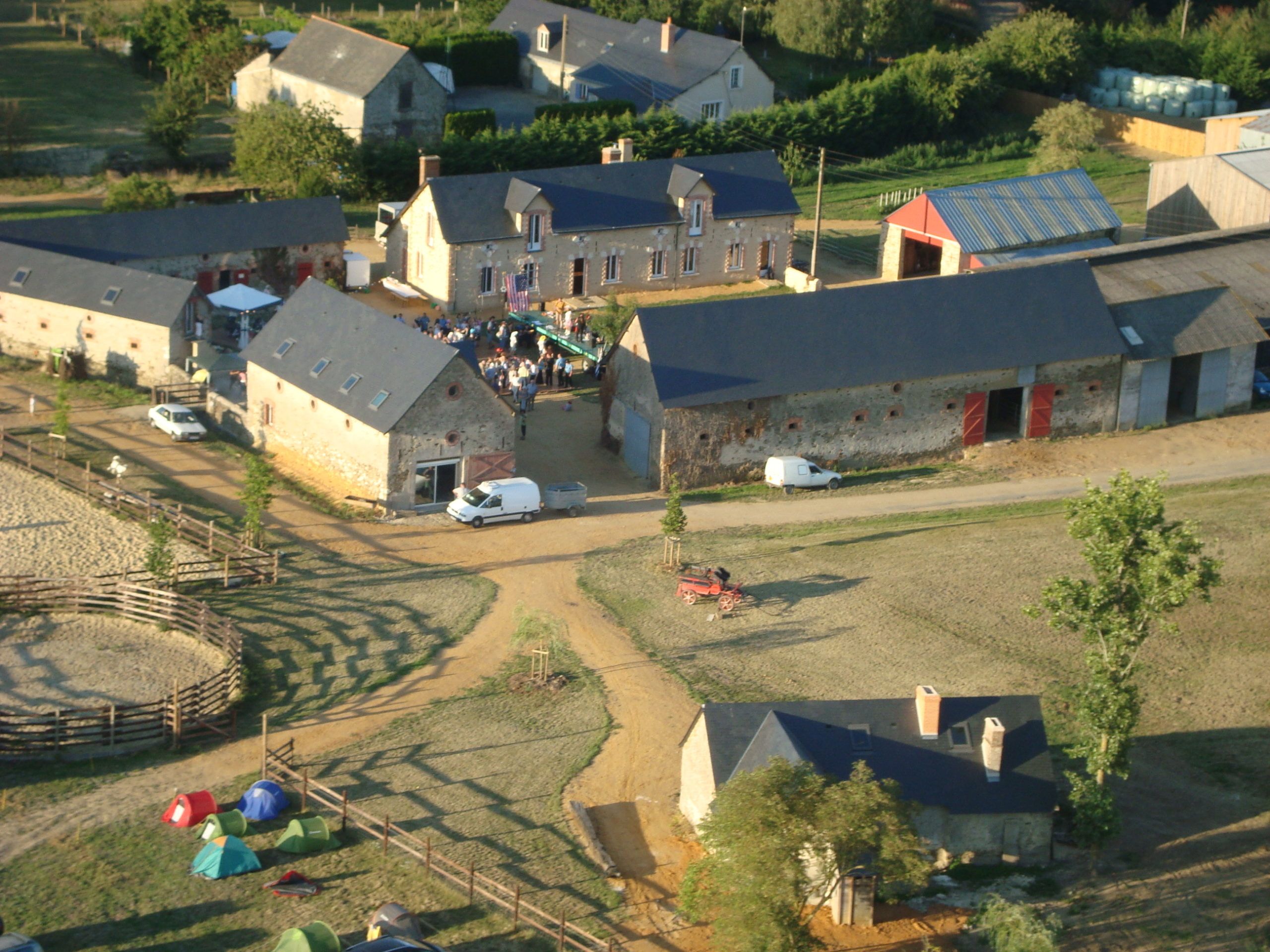 Vue aérienne du ranch : bâtiments en pierre, rond de longe, prés et tentes plantées près des gîtes